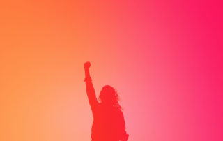 Silhouette of a woman holder her hand up in the air in a gesture of power