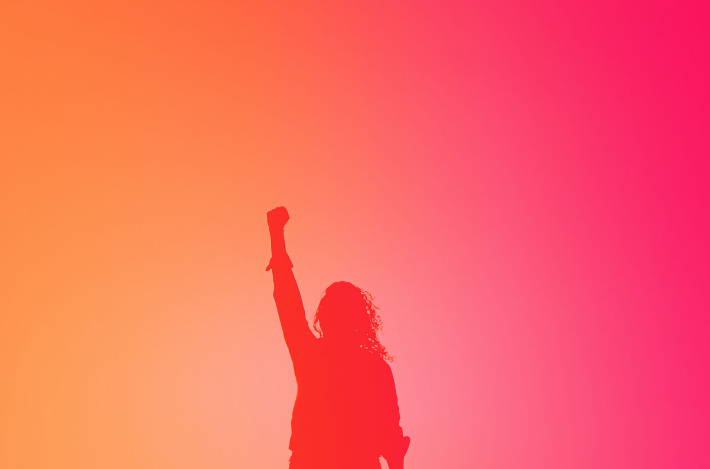 Silhouette of a woman holder her hand up in the air in a gesture of power