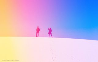 Two people stand atop a sand dune with nothing else in sight